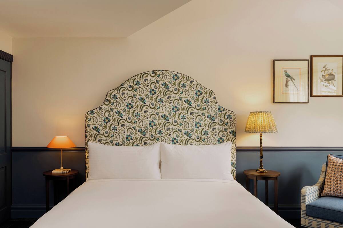 A neatly made bed with a patterned headboard, two bedside lamps, and framed artwork on the wall.