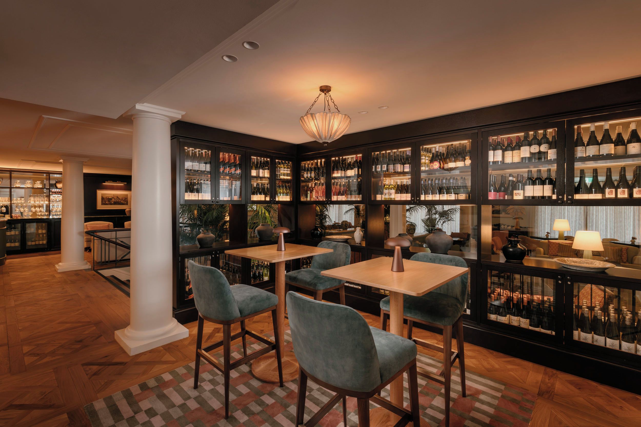 Zona de bar con diversas opciones de asientos, incluyendo taburetes y mesas, rodeada de estantes con botellas de vino.
