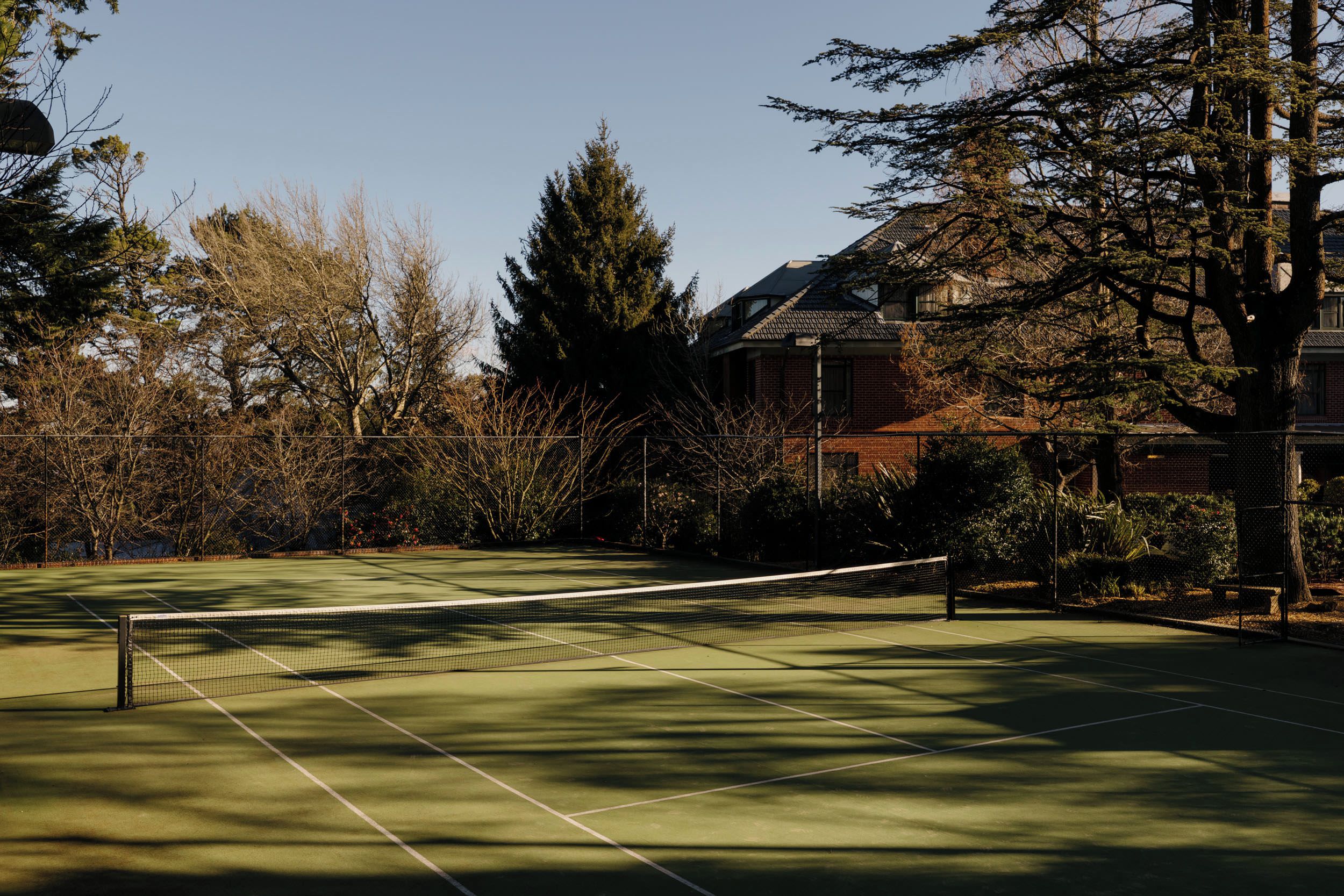 A tennis court with a net, surrounded by trees and a building.