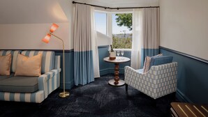 A corner room with a striped sofa, a patterned armchair, a small round table with a bottle and glasses, and a view through a window with curtains. - Ardour Lilianfels Blue Mountains (Katoomba)