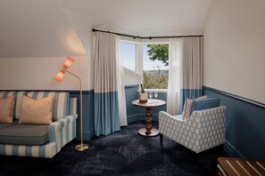 A corner room with a striped sofa, a patterned armchair, a small round table with a bottle and glasses, and a view through a window with curtains. - Ardour Lilianfels Blue Mountains (Katoomba)
