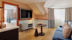 A modern hotel room with a TV mounted on the wall, a sofa, a small table with a lamp, and a dining area with a tray and a plate. - Ardour Lilianfels Blue Mountains (Katoomba)