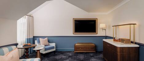 A hotel room with a sofa, armchair, small side table, and a wooden cabinet.