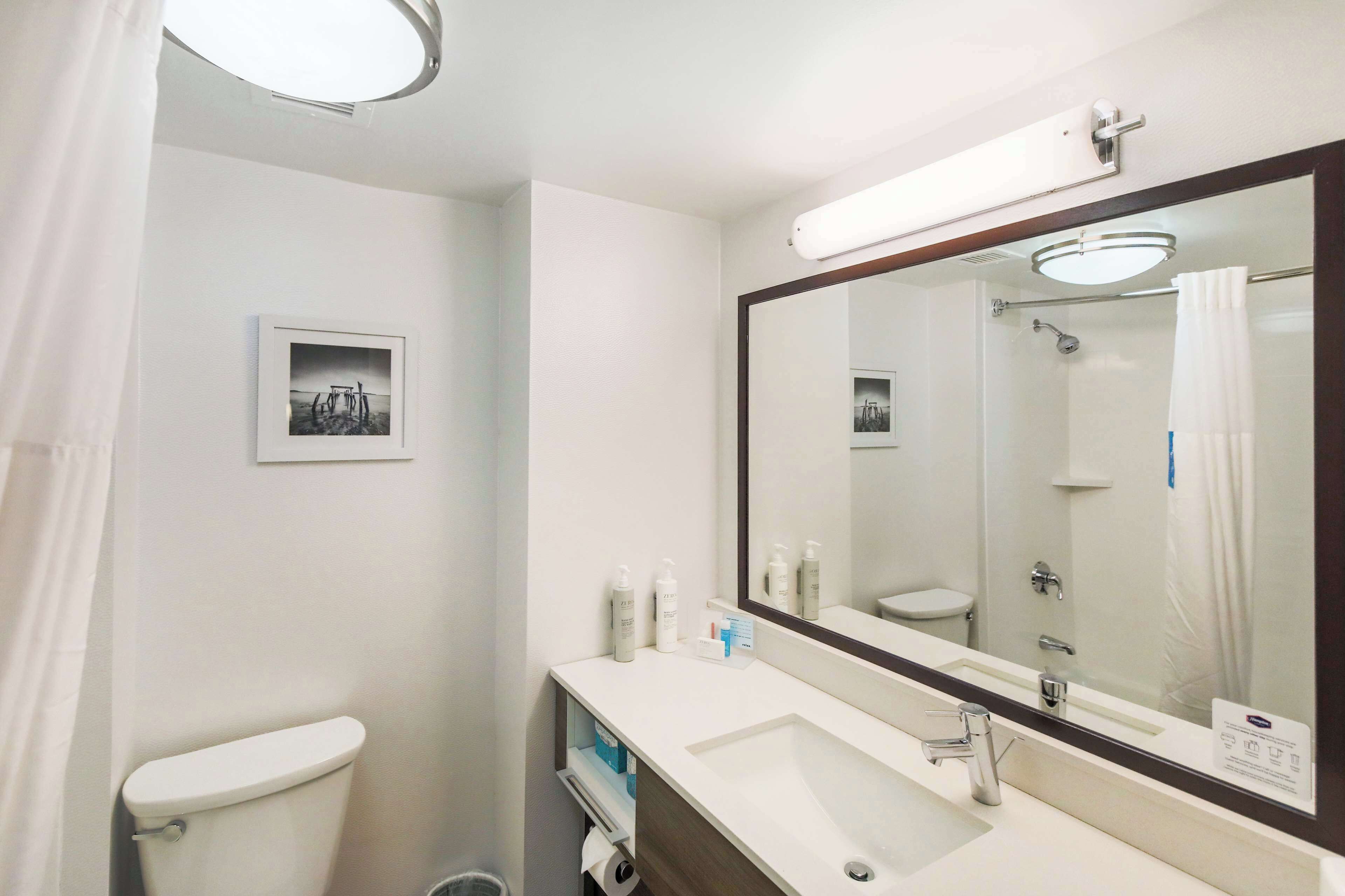 A bathroom with a toilet, sink, and mirror. There are toiletries on the sink counter.