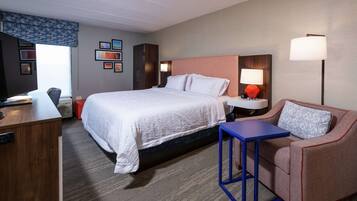 A hotel room with a large bed, a desk, a chair, a small table, and a sofa.