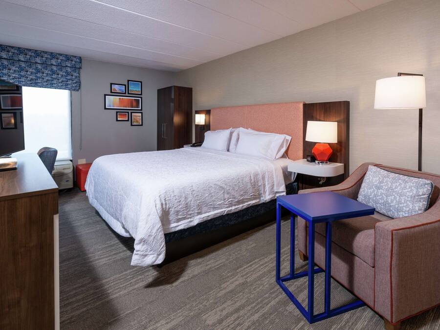 A hotel room with a large bed, a desk, a chair, a small table, and a sofa.