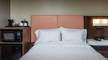 A hotel room with a bed, a microwave, a coffee maker, a mini fridge, and a bedside table with a lamp.