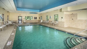 An indoor swimming pool with clear water, surrounded by lounge chairs and a tiled wall.
