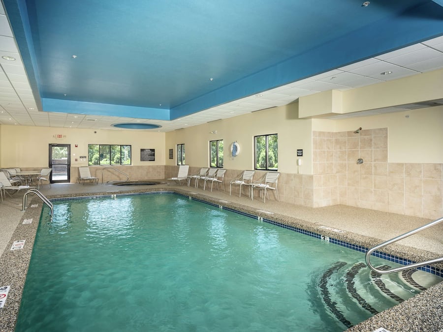 An indoor swimming pool with clear water, surrounded by lounge chairs and a tiled wall.