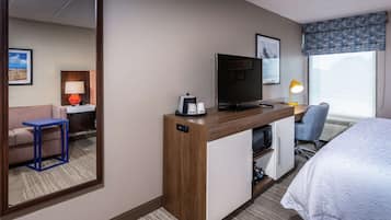 Habitación de hotel con cama, escritorio con televisor, silla, sofá, cafetera y lámpara.