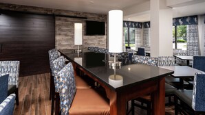 A modern restaurant with a long counter, patterned seating, and a flat-screen TV.