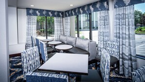 A modern hotel room with a sofa, two round tables, and patterned chairs.