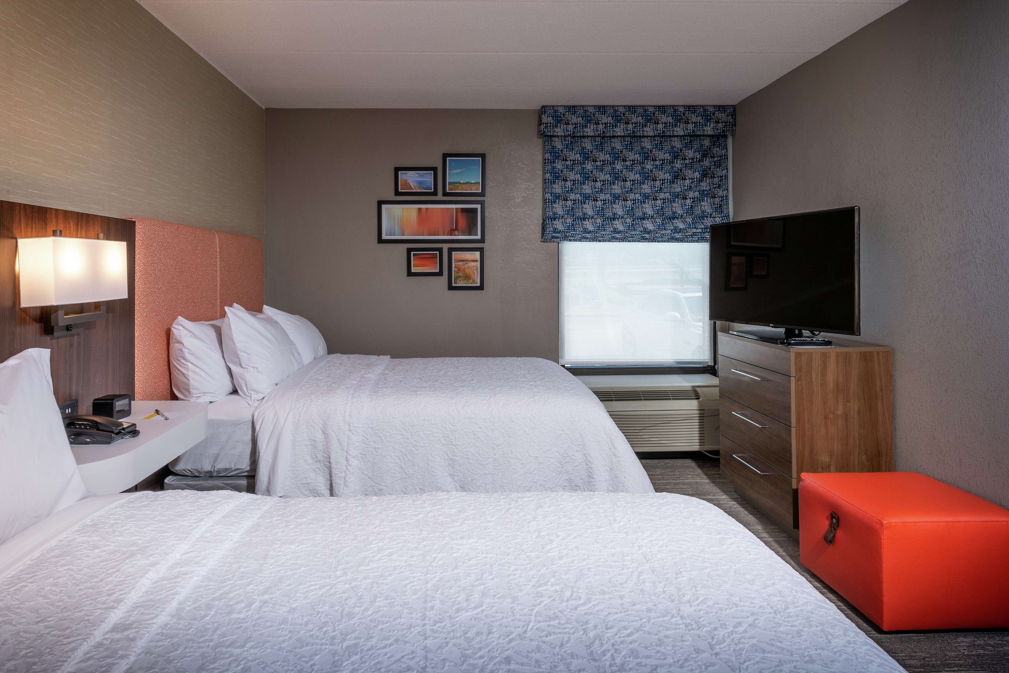A hotel room with two beds, a TV, a desk with a lamp, a dresser, and a window with a view.