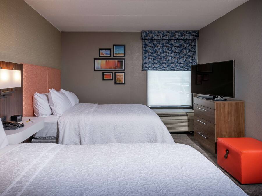 A hotel room with two beds, a TV, a desk with a lamp, a dresser, and a window with a view.