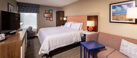 A hotel room with a bed, a desk, a chair, a sofa, and a TV.