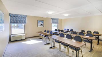 Una sala conferenze con diversi tavoli e sedie, un'ampia finestra con persiane e un quadro appeso al muro.