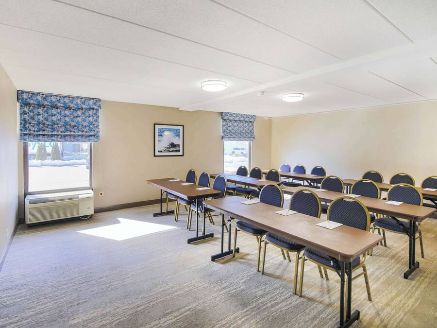 A conference room with multiple tables and chairs, a large window with blinds, and a picture on the wall.
