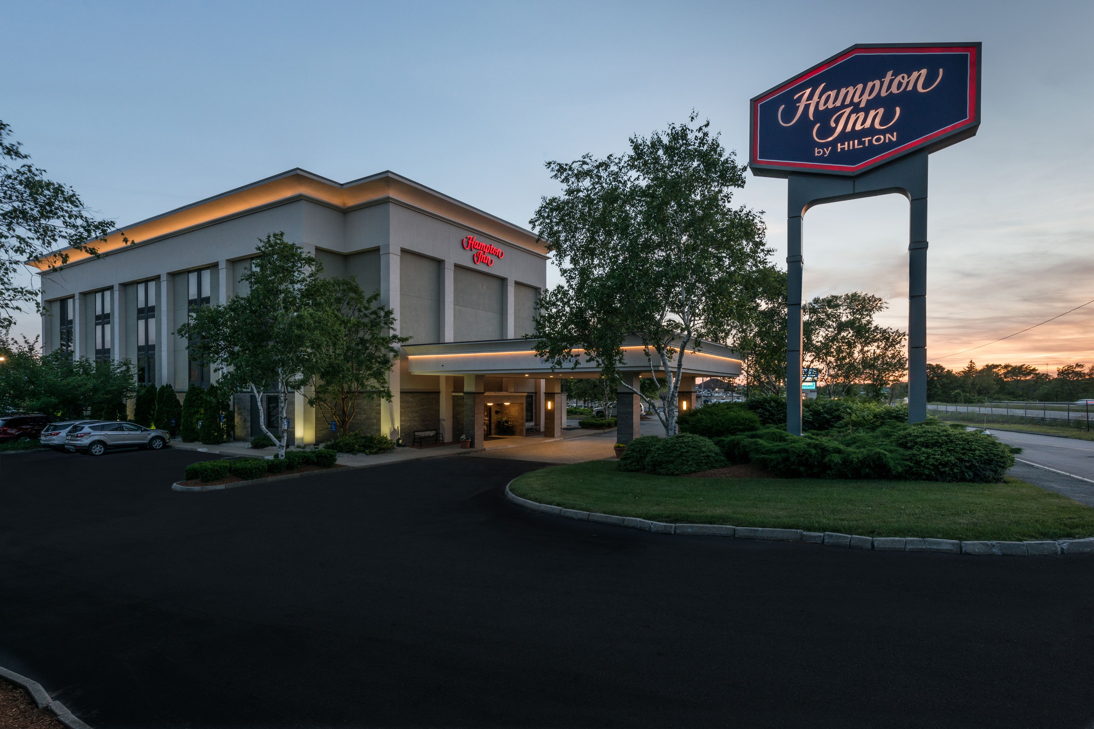 Een Hampton Inn by Hilton hotel met een moderne gevel, een goed verlichte ingang en een groot bord.