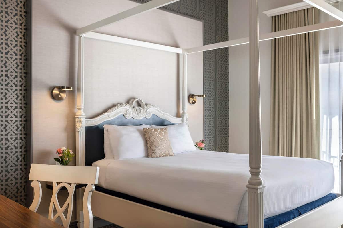 A four-poster bed with a white headboard, a bedside table, and a nightstand with a vase of flowers.