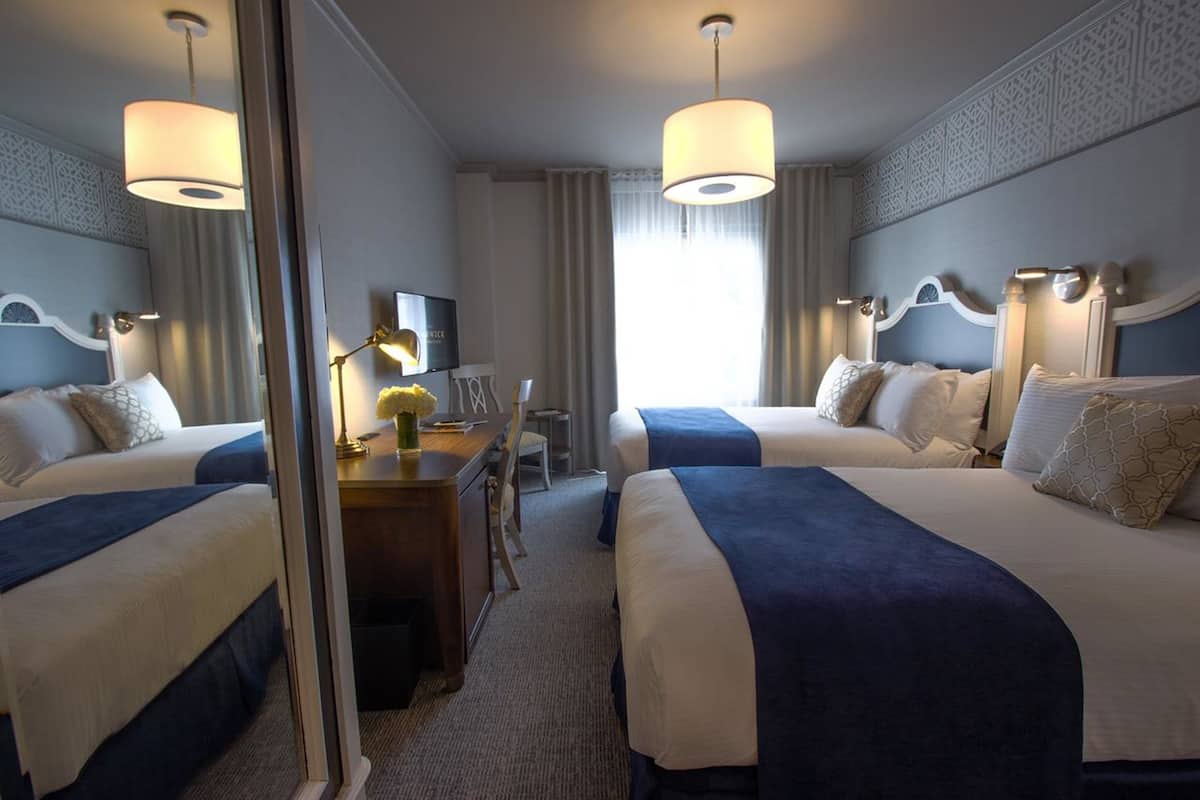 A hotel room with two beds, a desk with a lamp, a television, and a mirror.