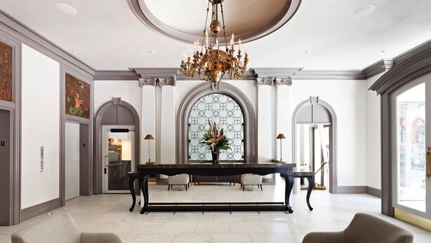 A spacious lobby with a grand chandelier, a long dining table, and comfortable seating.