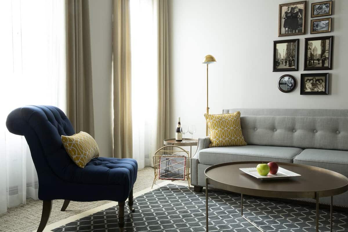 A living room with a blue armchair, a grey sofa, a coffee table with apples, and a floor lamp.