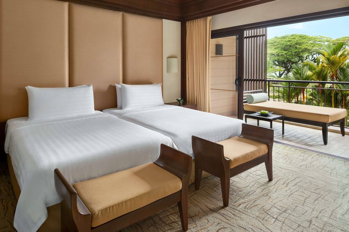 A hotel room with two beds, a small balcony with a table and chairs, and a view of palm trees.