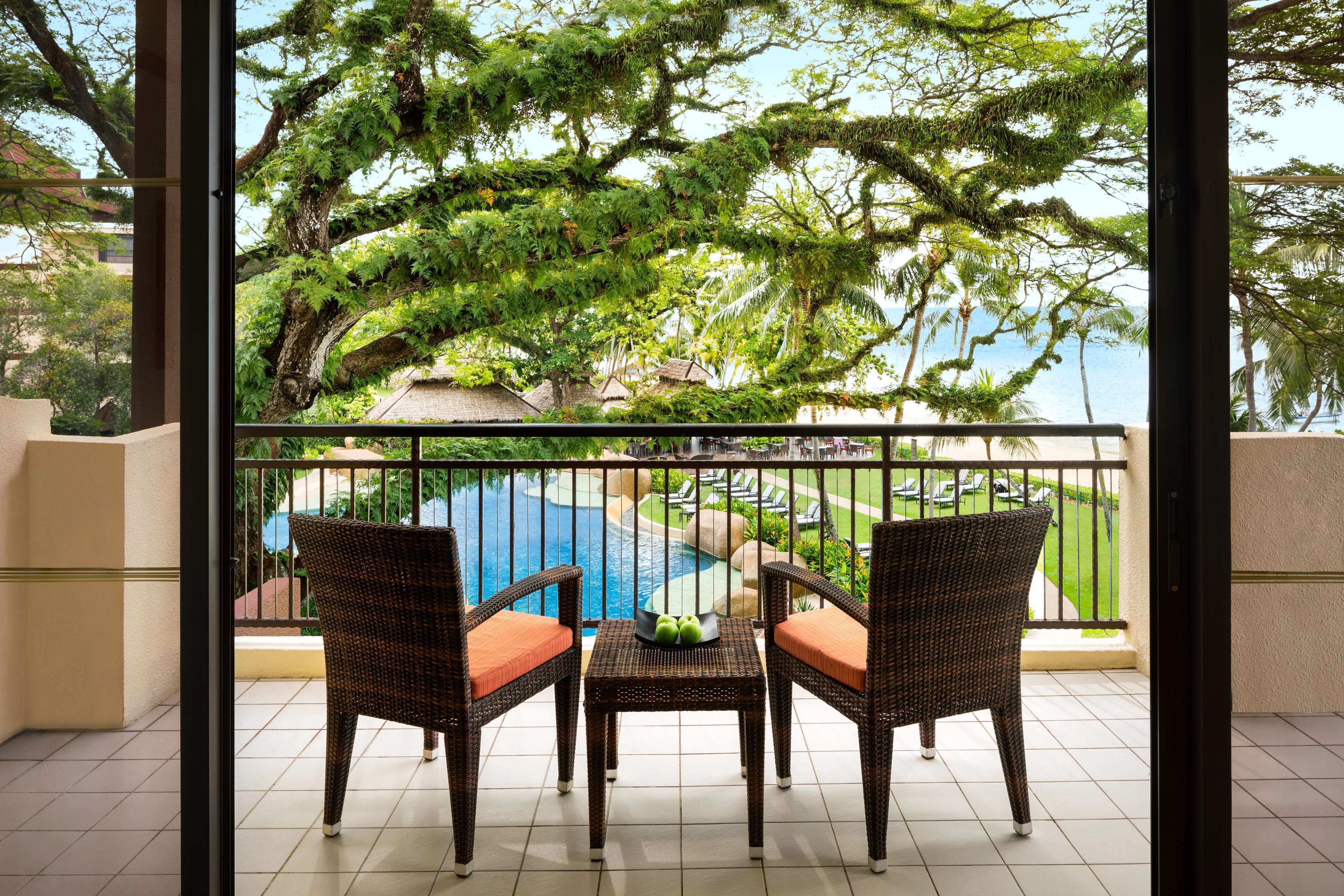 A balcony with wicker furniture and a view of a pool and greenery.