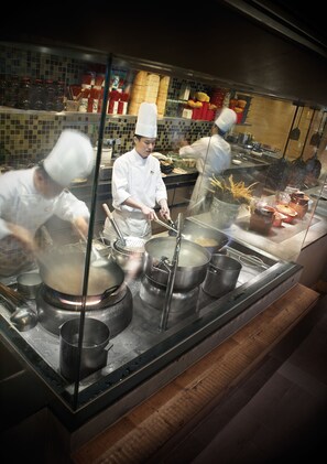 A kitchen with chefs working, stainless steel pots, and a tiled backsplash.