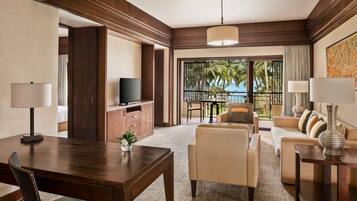 A hotel room with a dining area, a sofa set, a TV, and a balcony with a view of palm trees.