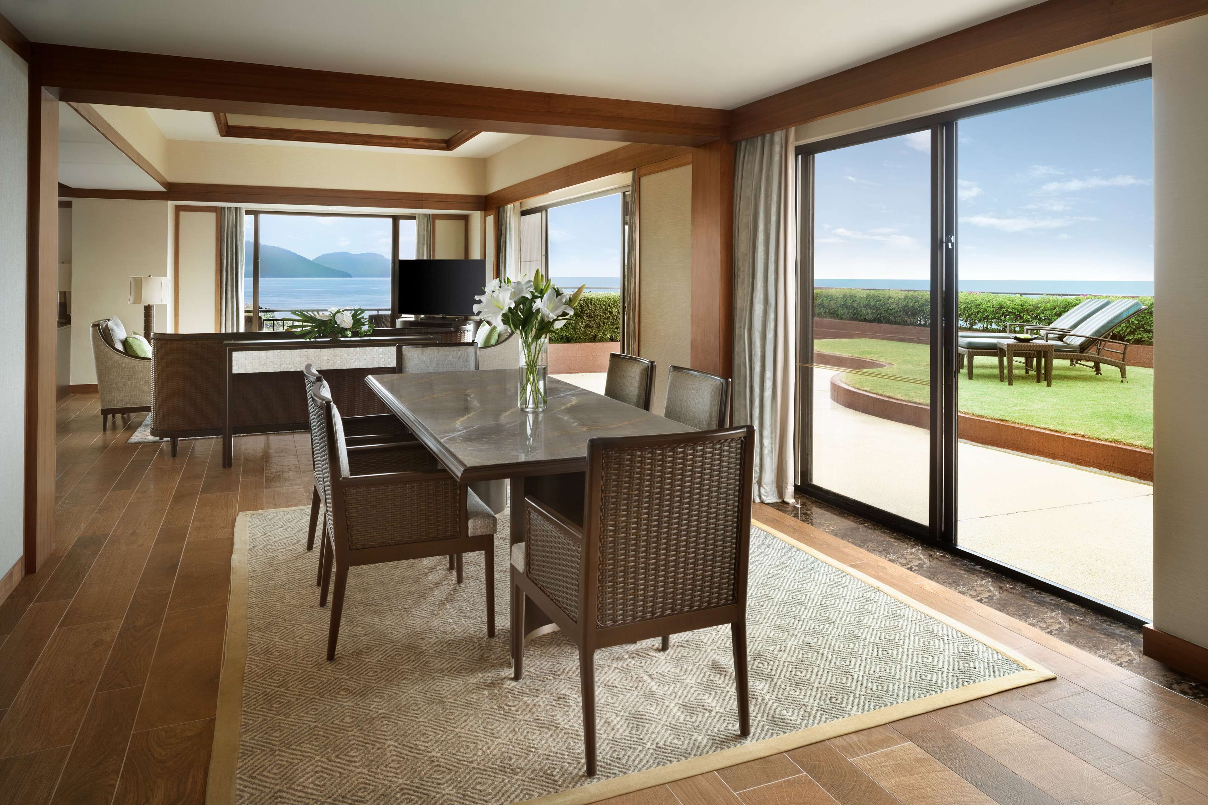 A spacious dining area with a large table and chairs, a television, and a view of the ocean through large sliding doors.