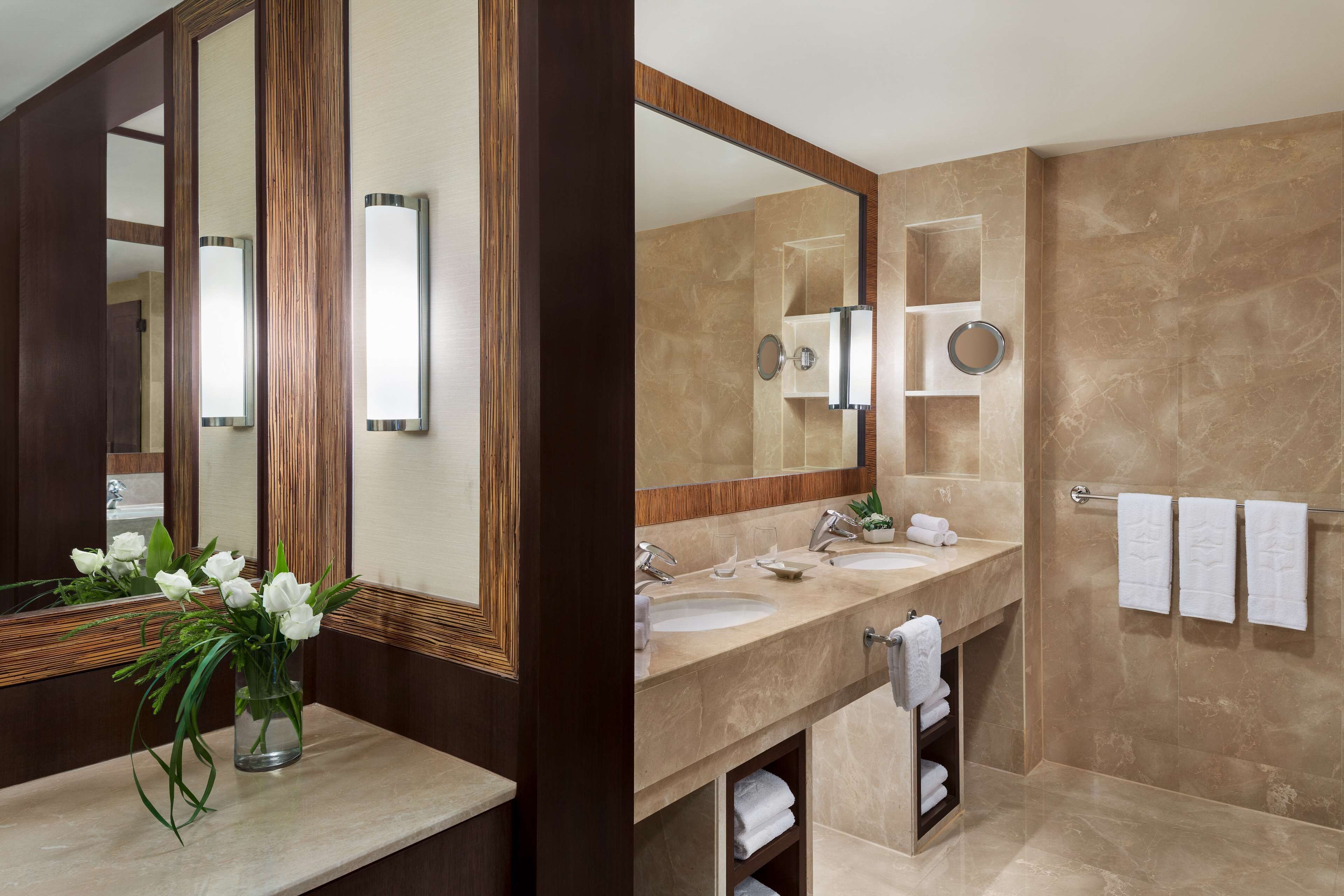 A modern bathroom with two sinks, a large mirror, and a vanity with a vase of flowers.