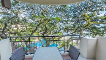 A balcony with a table and chairs, overlooking a pool and lush greenery.