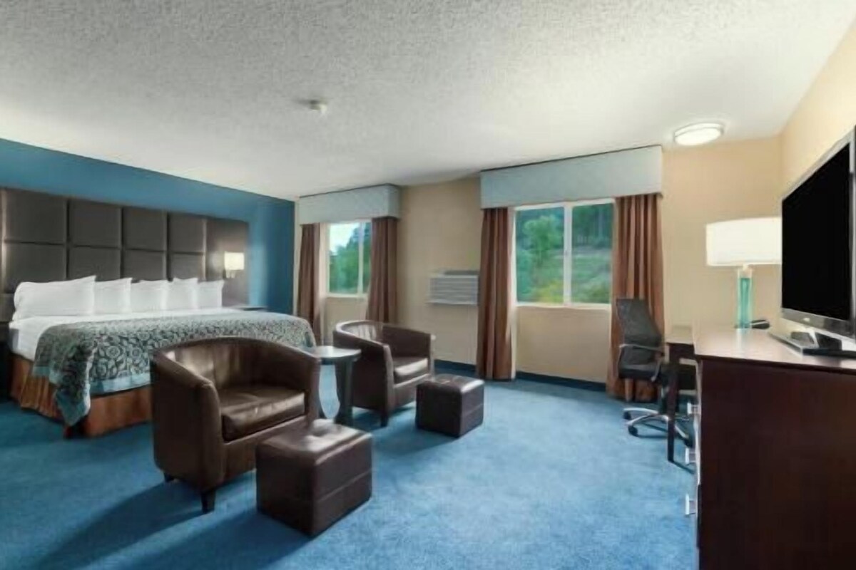 A hotel room with a bed, two armchairs, a desk, and a television.