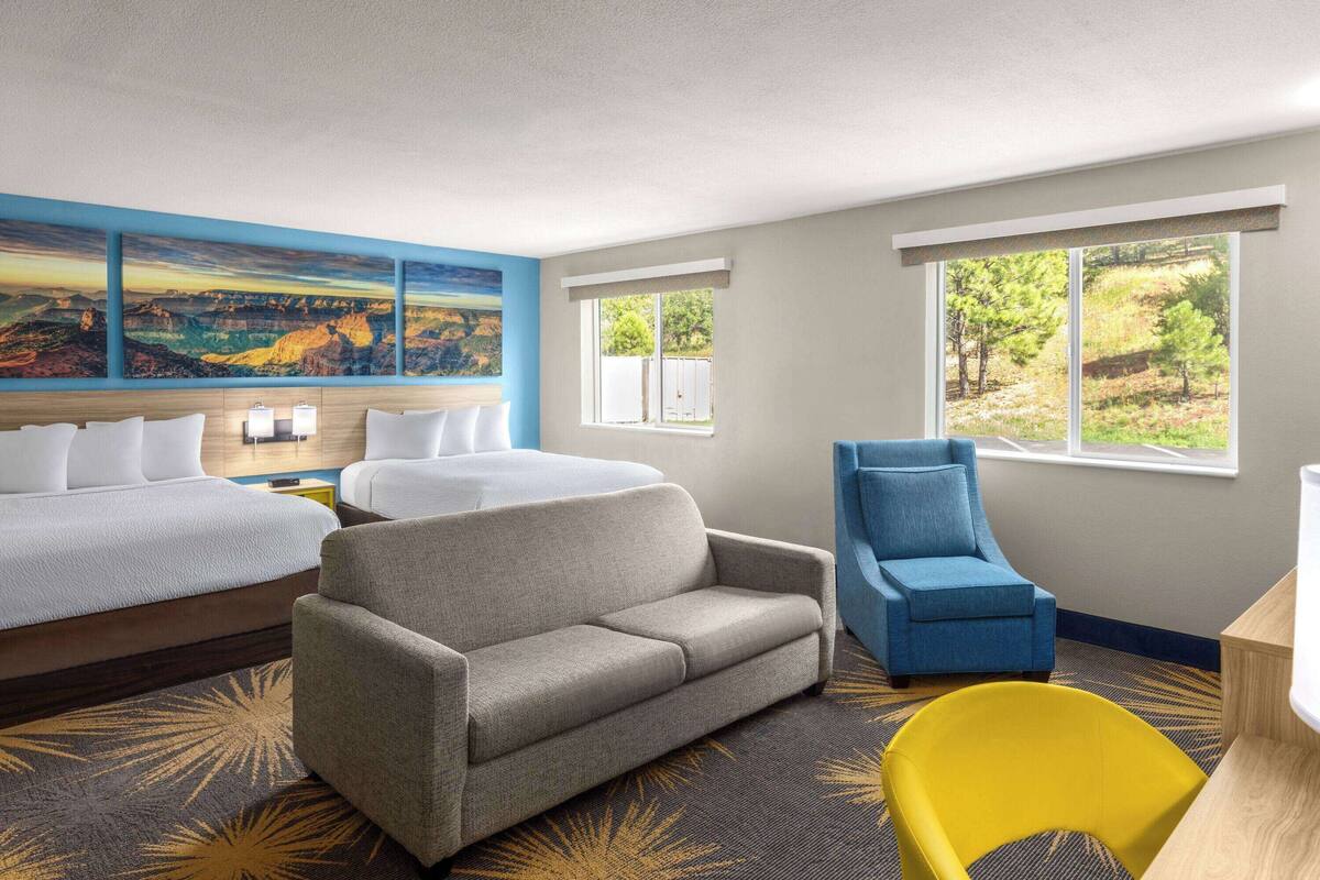 A hotel room with a bed, two sofas, a yellow chair, and a large window with a view of trees.