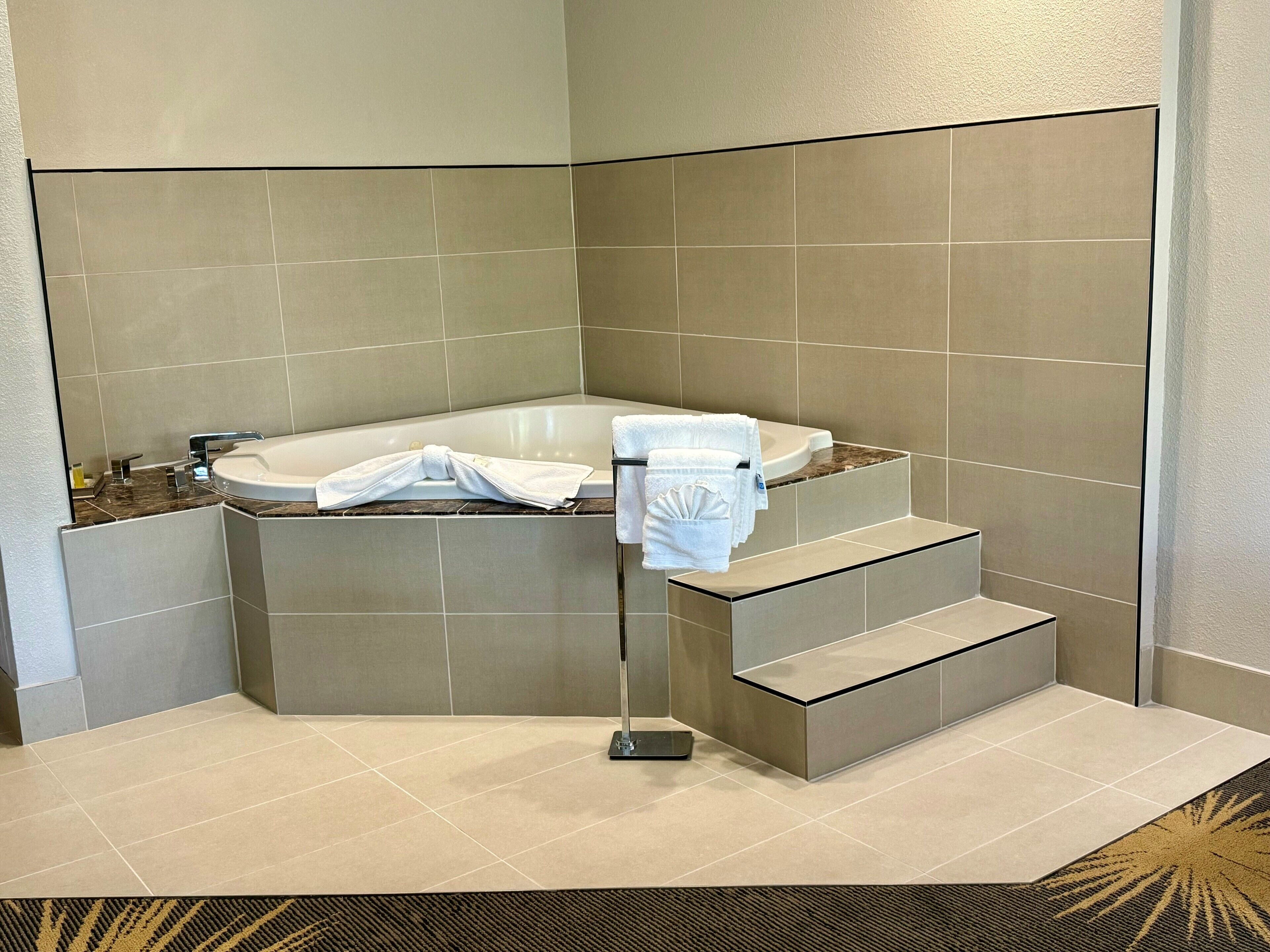A corner bathroom with a bathtub, a sink, and a towel rack with towels.
