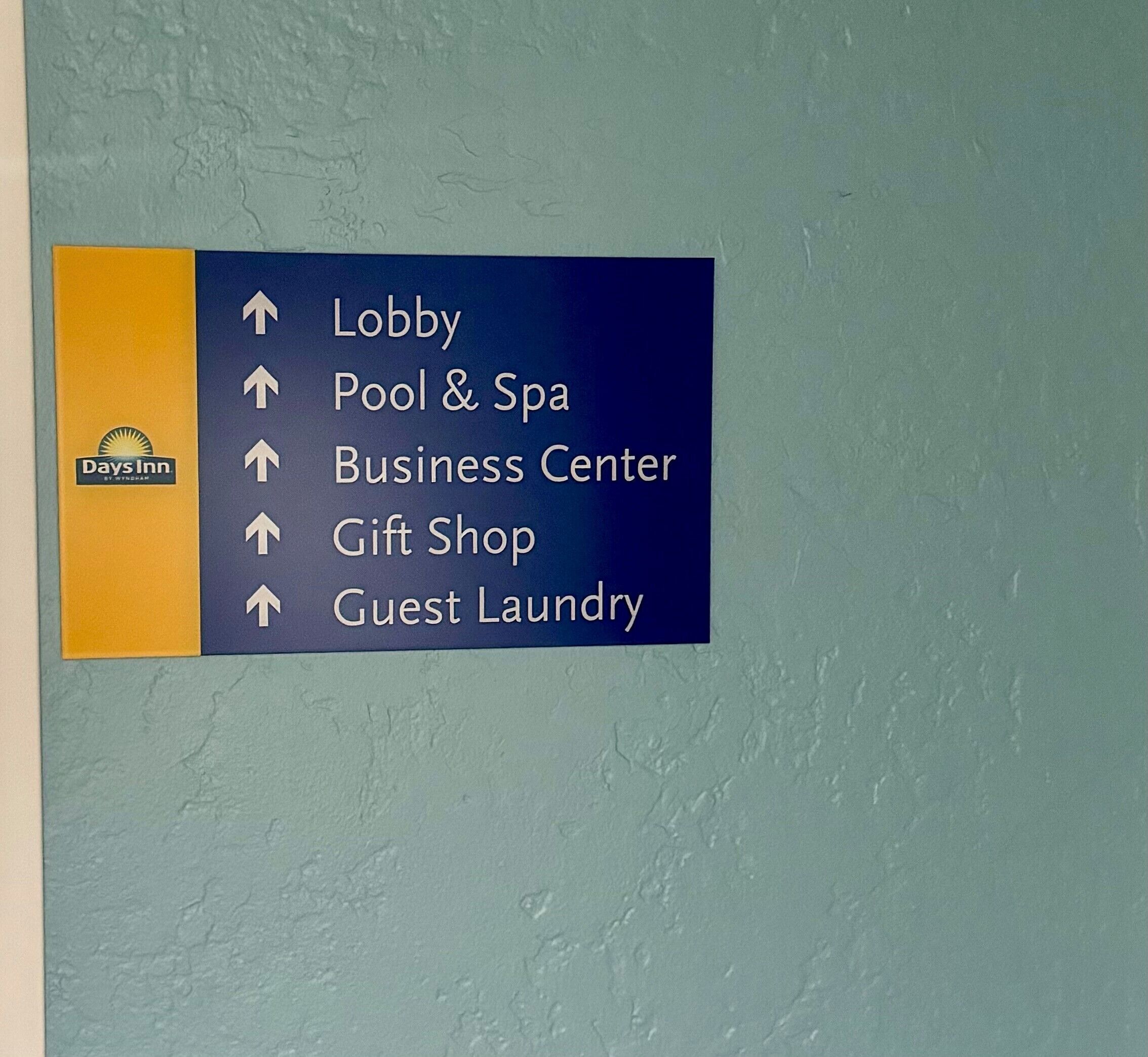 Egy irányjelző tábla, amely nyílakkal mutatja a hotel különböző szolgáltatásait, mint például a recepciónál található pihenőteret, az úszómedencét és a wellness-központot, az üzleti központot, az ajándékboltot és a vendégek számára fenntartott mosodát.