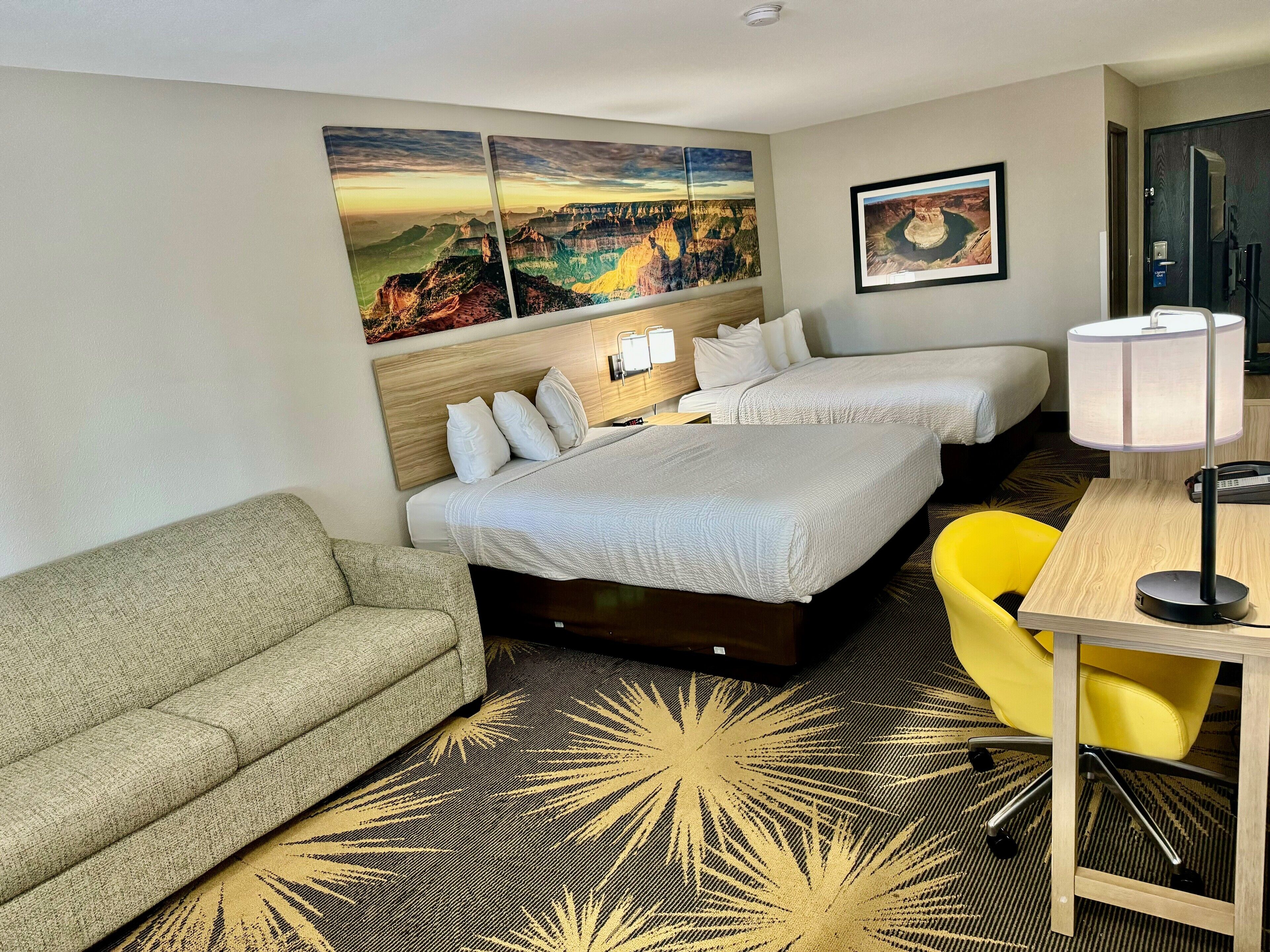 Habitación de hotel con dos camas, un sofá, un escritorio con lámpara y obras de arte en las paredes.