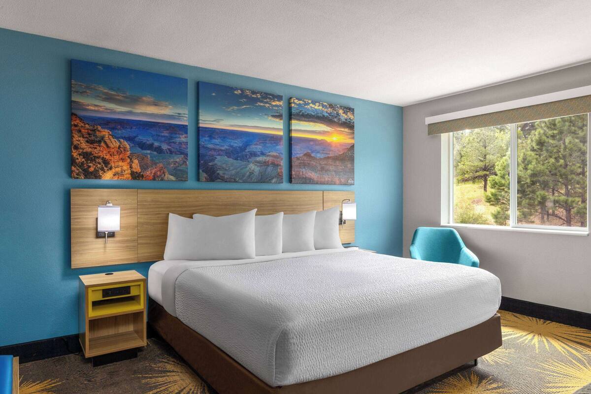 A hotel room with a large bed, a nightstand, a chair, and a window with a view of trees.