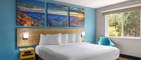 A hotel room with a large bed, a nightstand, a chair, and a window with a view of trees.