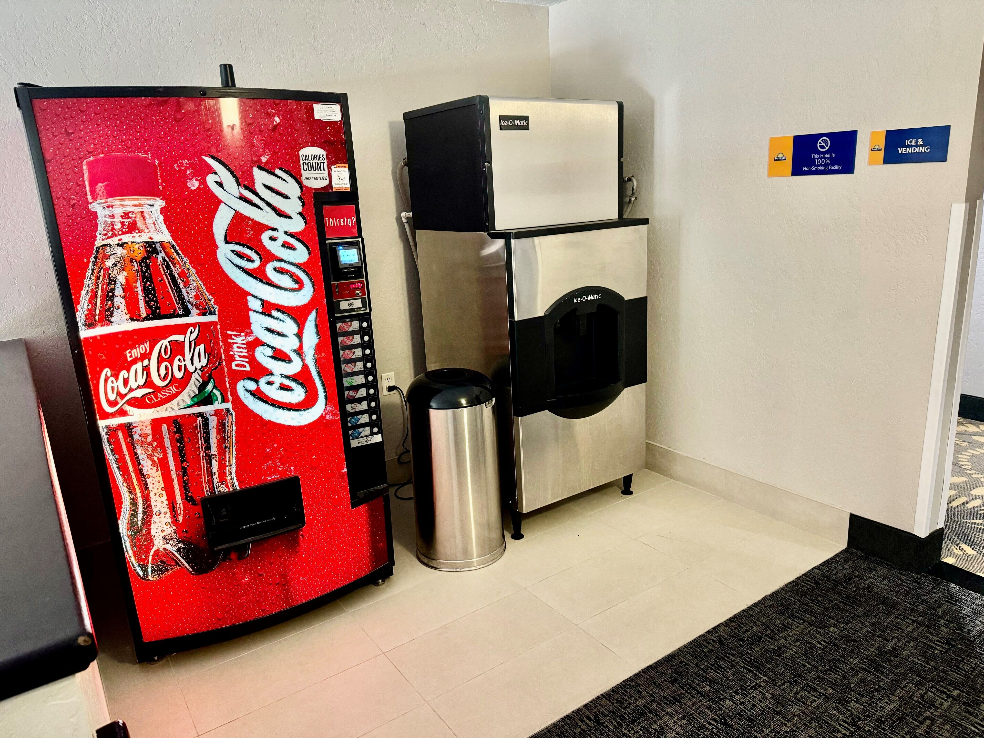 Una máquina expendedora de Coca-Cola, un refrigerador pequeño y un cubo de basura en el vestíbulo de un hotel.