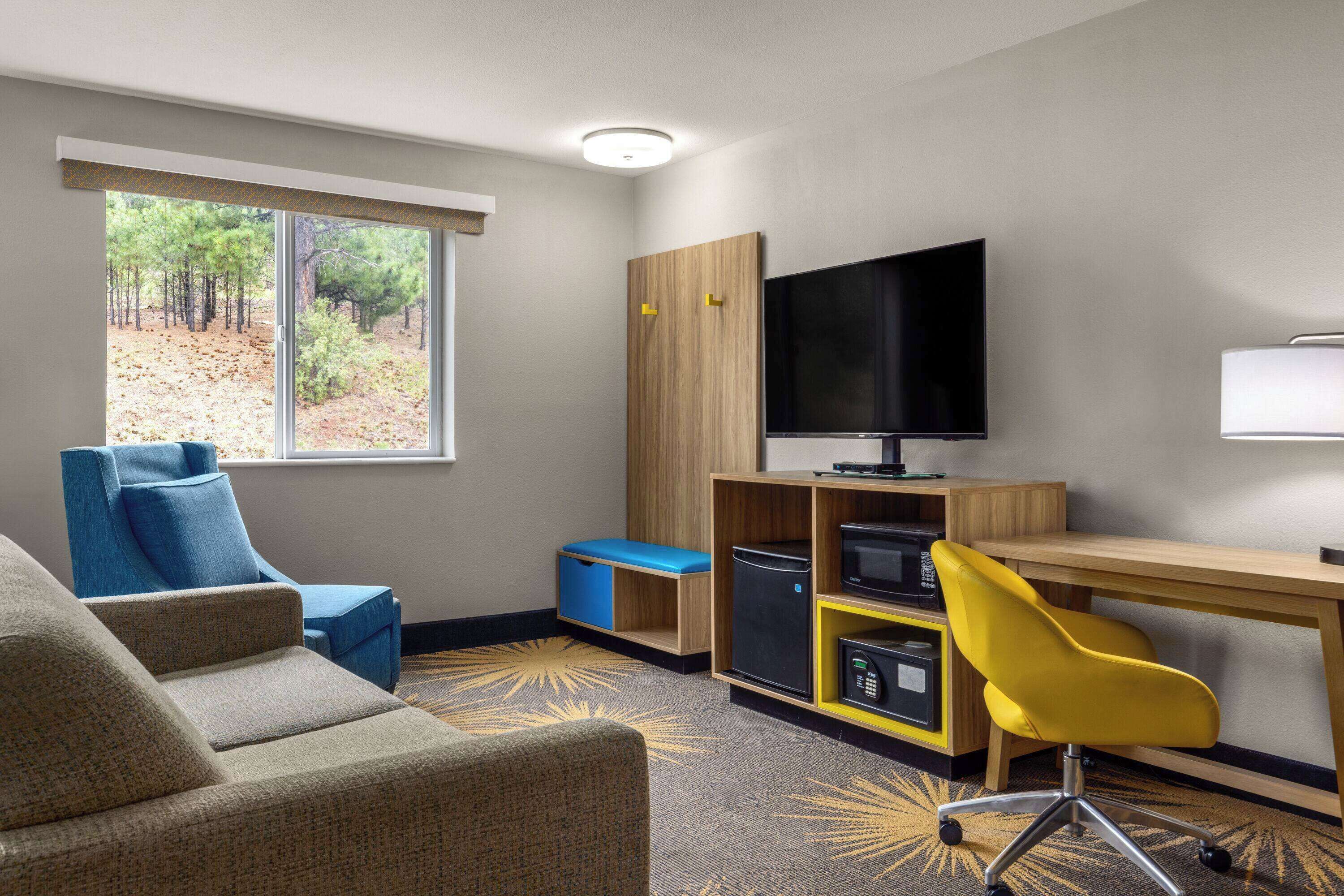 Une chambre d’hôtel avec un canapé, un bureau, une télévision et une vue sur les arbres par la fenêtre.