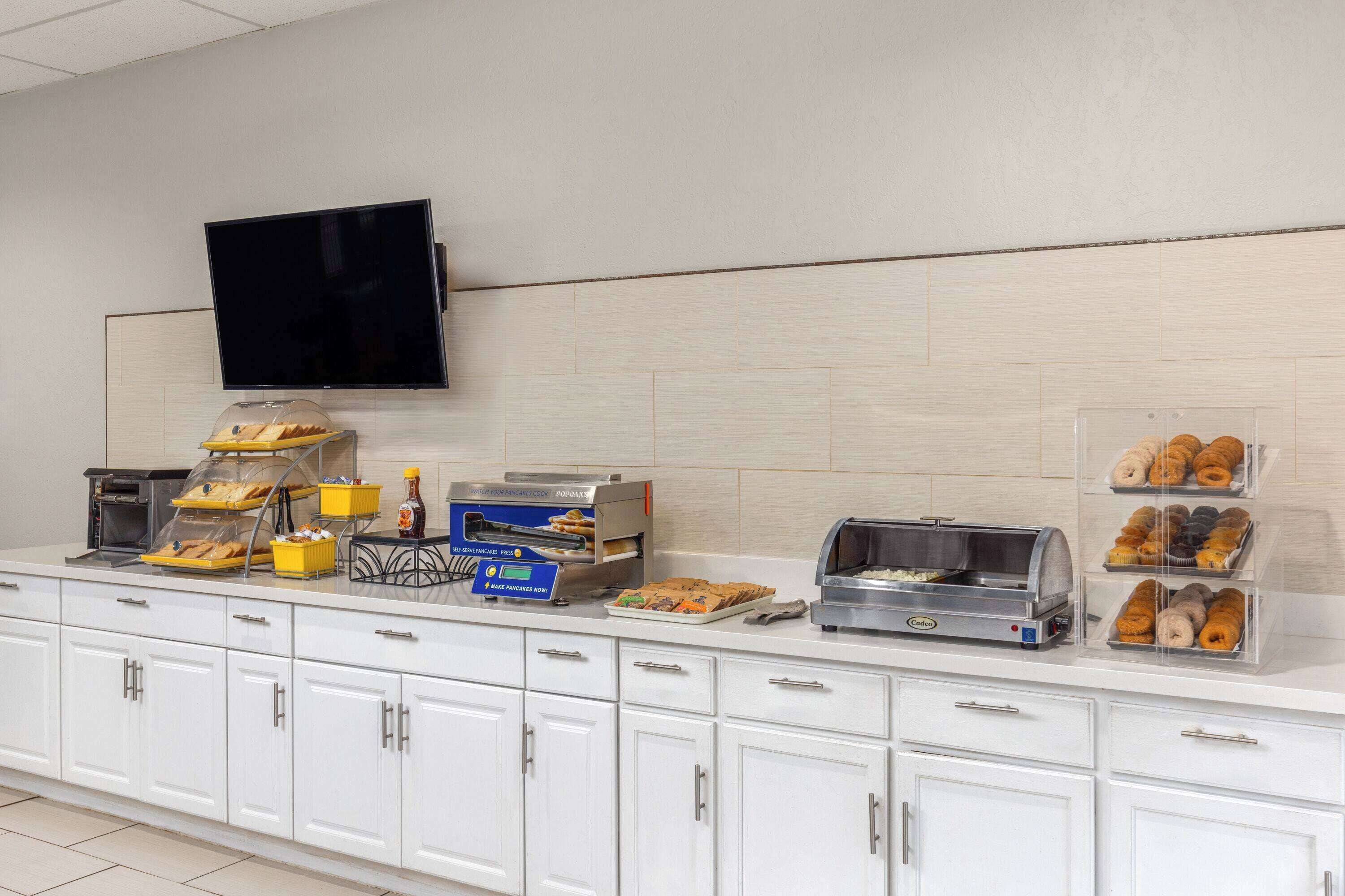 A breakfast buffet with various food items, a coffee machine, and a TV mounted on the wall.
