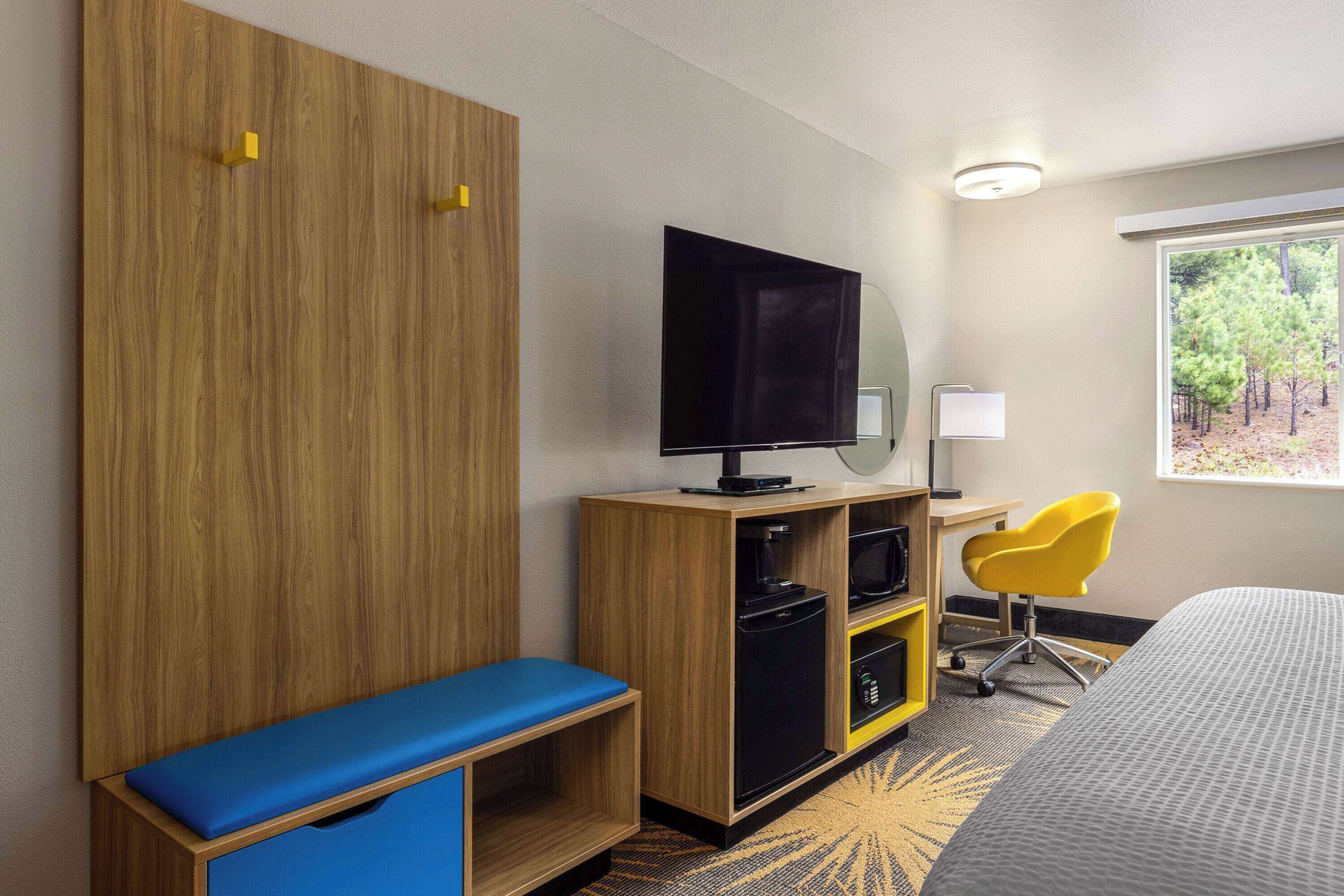 Une chambre d’hôtel comprenant un lit, une télévision, un bureau avec une chaise, une armoire et une fenêtre donnant sur des arbres.