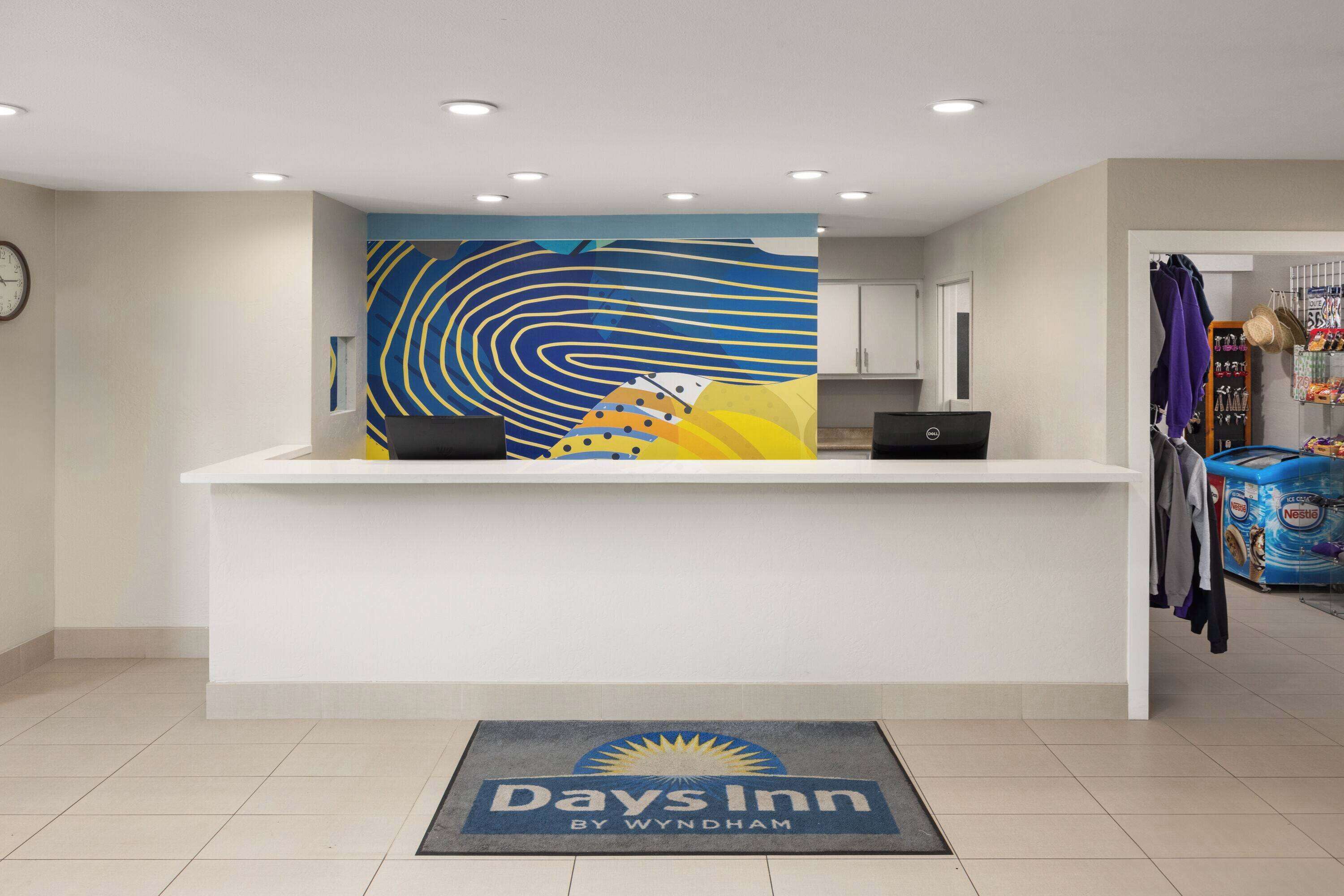 Un área de recepción con un mostrador, un reloj y una pared con un diseño abstracto y colorido.