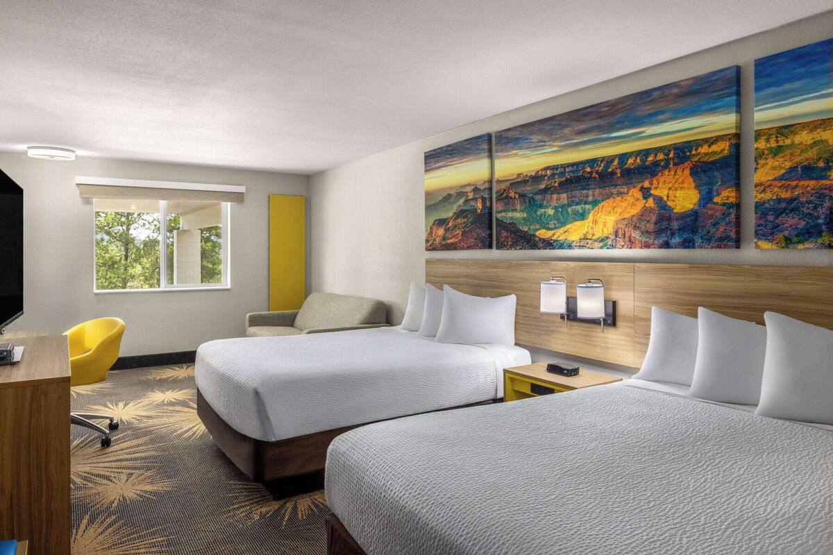 A hotel room with two beds, a desk, a chair, a window, and a large painting on the wall.