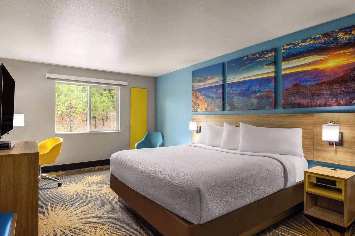 A hotel room with a large bed, a desk, a chair, a window with a view of trees, and a wall with three paintings.