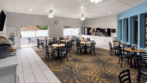 A dining area with multiple tables and chairs, a kitchen area, and a clock on the wall.