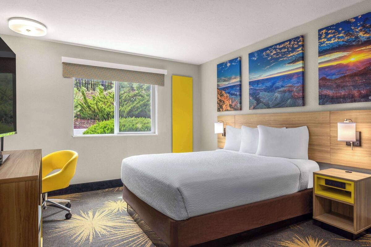 A hotel room with a large bed, a desk, a chair, and a window with a view of greenery.