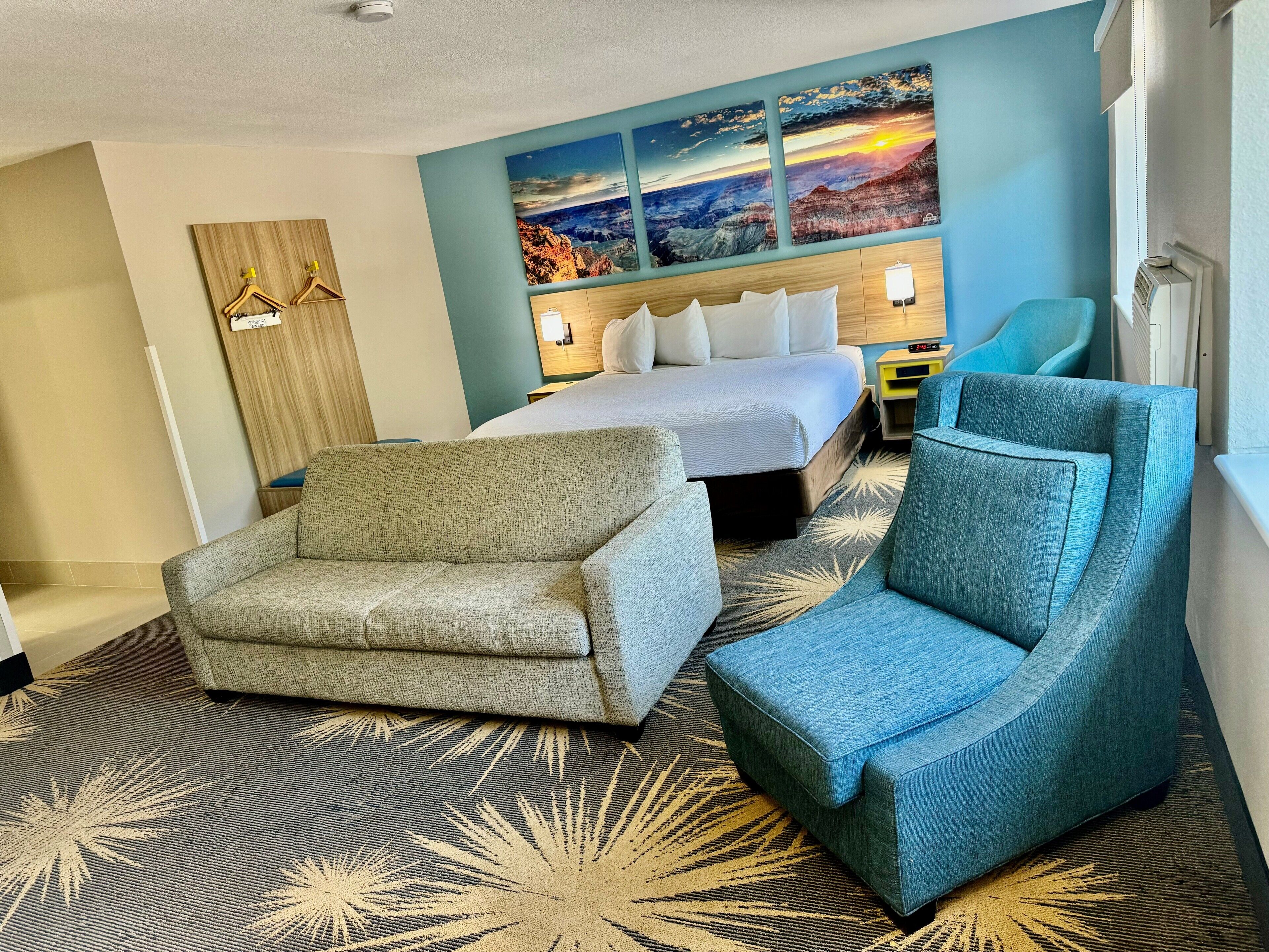 Une chambre d’hôtel comprenant un lit, deux fauteuils, un bureau et un téléviseur fixé au mur.